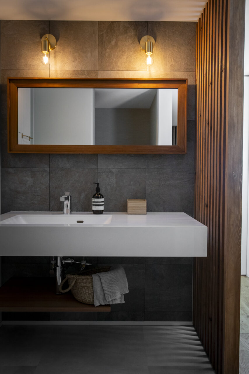 木製フレームの横長ミラーと間接照明が映える、タイル壁の造作洗面台空間